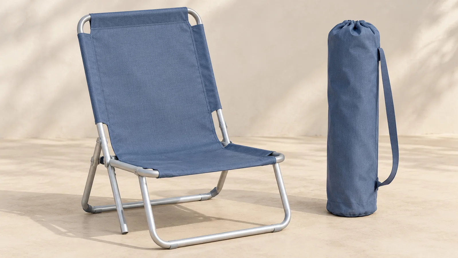 Una sencilla silla de playa plegable abierta junto a su bolsa de transporte a juego.
